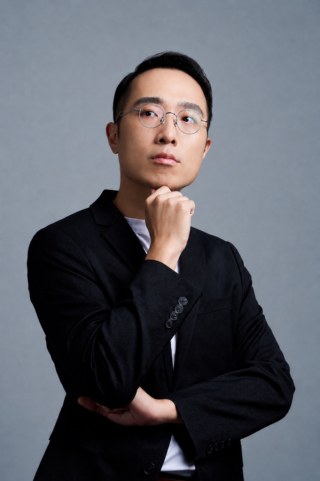 林思翰講師形象照，身穿黑色西裝、手托下巴思考